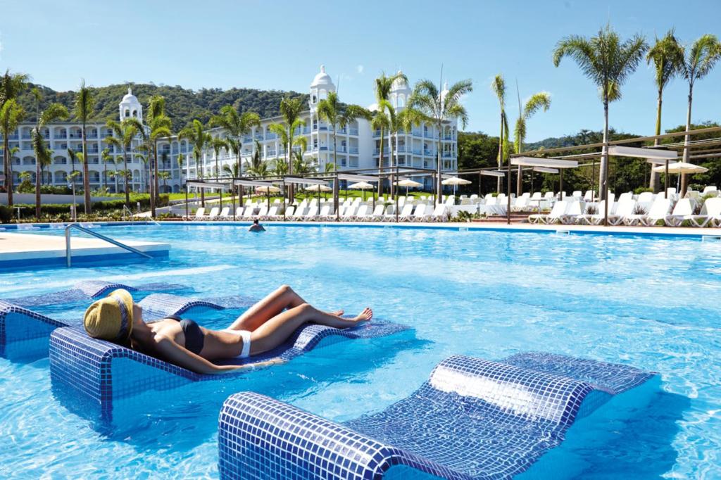 a woman laying on a raft in a swimming pool at a resort at Riu Palace Costa Rica - All Inclusive in Coco