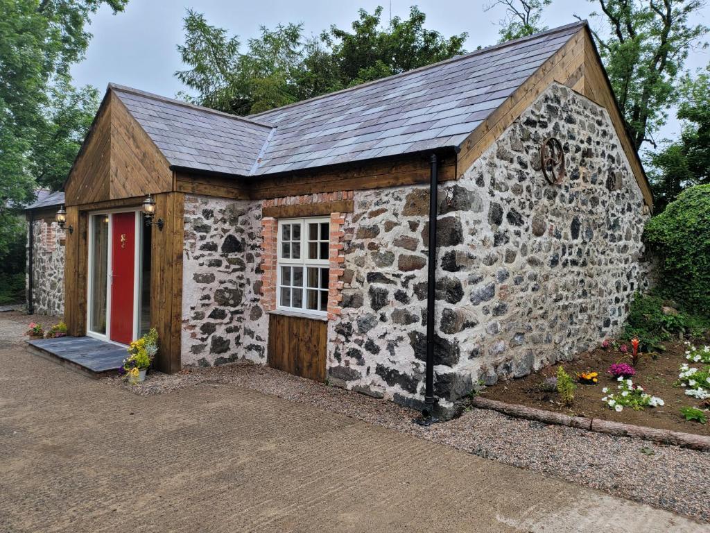 un pequeño edificio de piedra con una puerta roja en Hare Cottage, en Ballymena