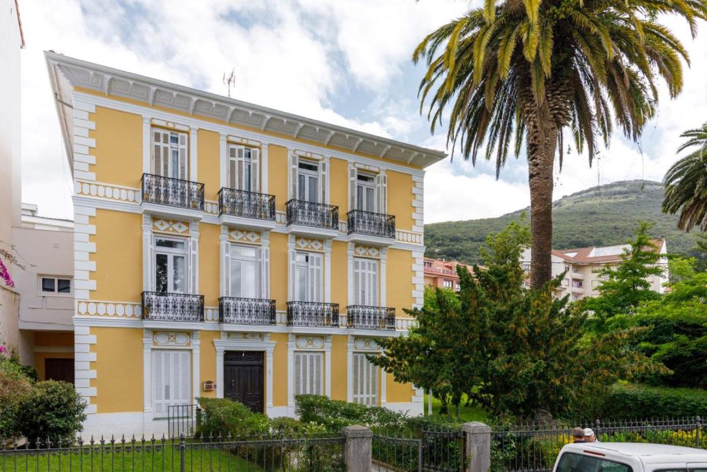 a yellow house with a palm tree in front of it at Apartamentos CASA CARRE 1893 in Santoña