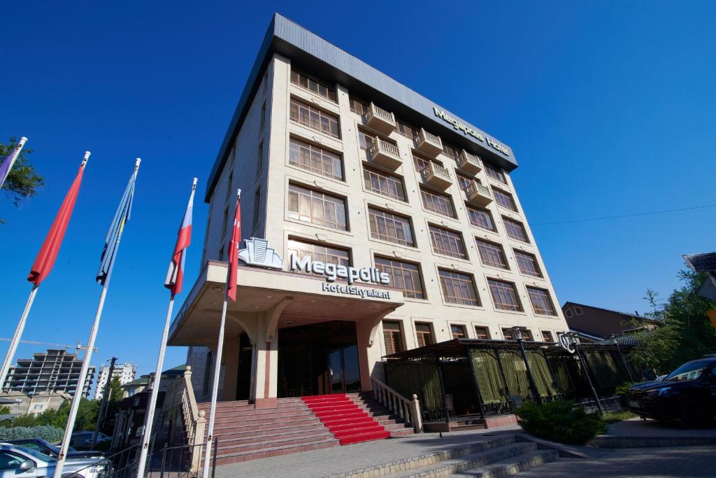 a large white building with flags in front of it at Megapolis Hotel Shymkent in Shymkent