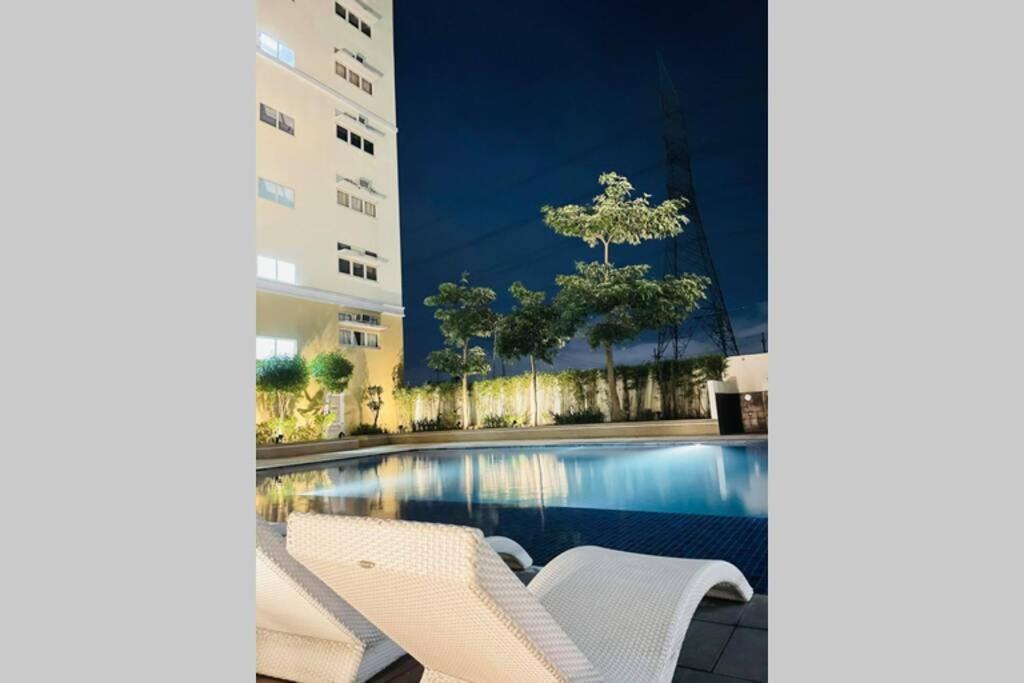 a swimming pool with two white chairs next to a building at Cozy Studio Type Condo with Pool in Biñan
