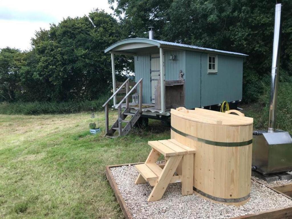 a small blue house with a bench and a barrel at Charming Shepherds Hut with Wood Fired Hot Tub in Charlton Musgrove