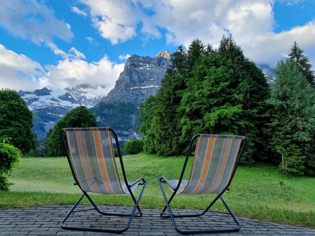 格林德瓦的住宿－MOM - Alpine Boutique Apartments, Grindelwald gletscher, Eiger View Terrace Studio，两把椅子在山前,彼此相邻