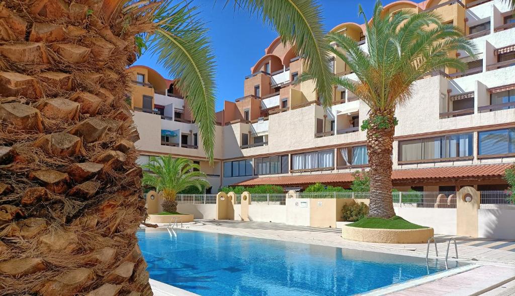 un complexe avec une piscine bordée de palmiers et un bâtiment dans l'établissement Charmant Appartement vue PORT DE GRUISSAN 5DROM44K, à Gruissan