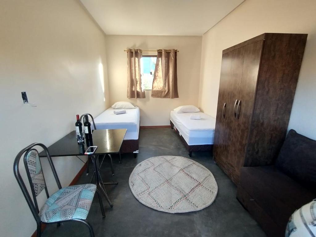 ヴァレ・ド・カパオンにあるChalés Vila Bela Vale do Capãoのベッド2台、テーブル、椅子が備わる小さな客室です。