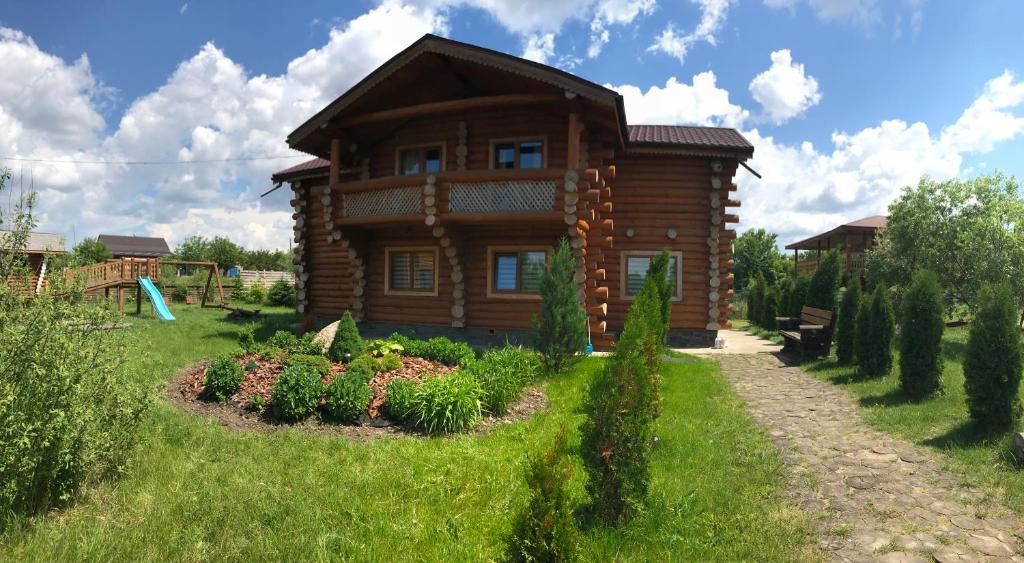 une maison en rondins avec un jardin en face de celle-ci dans l'établissement Cottage Radomyshl', à Radomyshlʼ