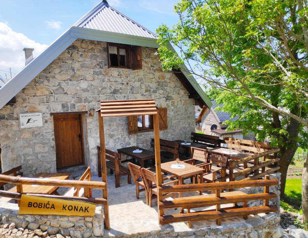 una casa de piedra con mesas de madera y sillas delante de ella en Bobića konak - Lukomir, en Lukomir