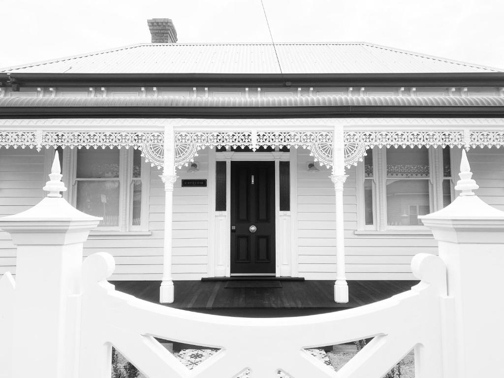 une maison blanche avec une porte noire et une terrasse couverte dans l'établissement Castlebar - Superior Boutique Accomodation - Steps to Pakington Street, à Geelong West