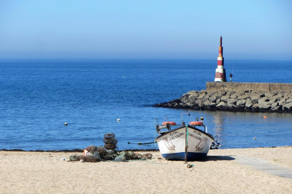 a boat sitting on the beach with a lighthouse at Casa do Remo Praia da Aguda in Arcozelo