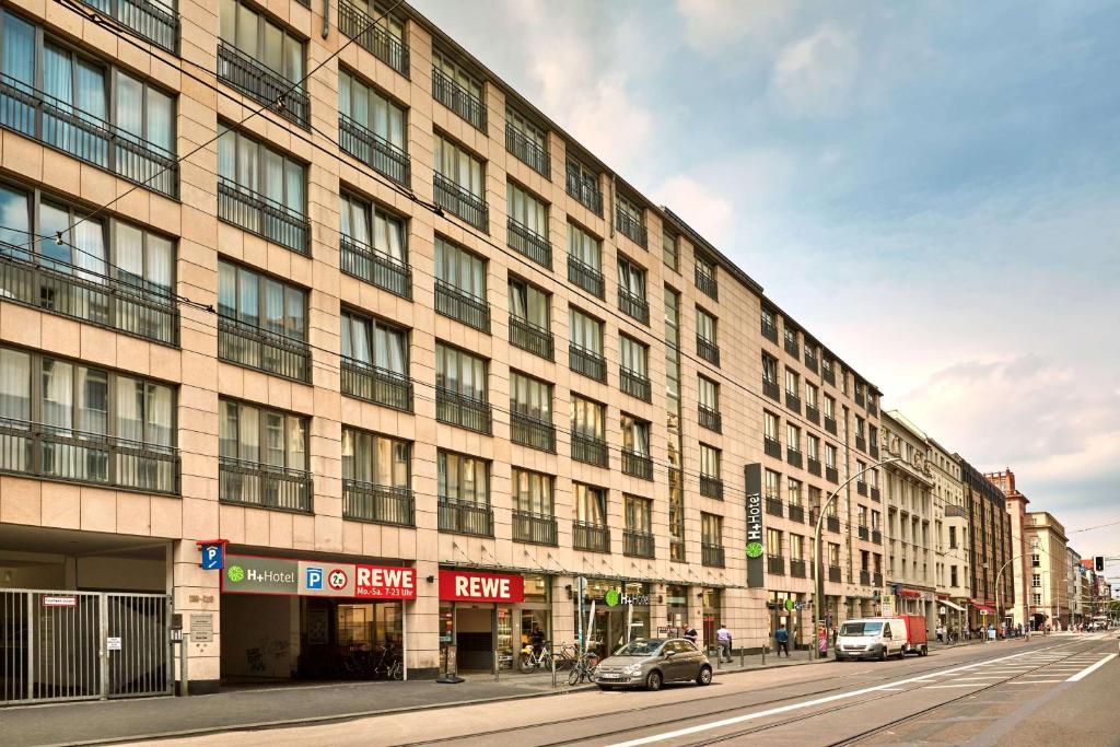 ein großes Gebäude an einer Stadtstraße mit draußen geparkt in der Unterkunft H+ Hotel Berlin Mitte in Berlin