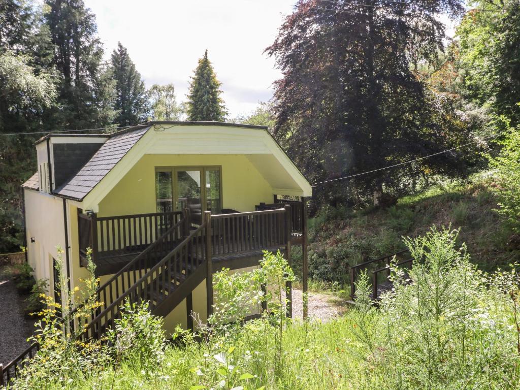 een klein geel huis met een terras in het bos bij Waterfall Apartment in Inverness