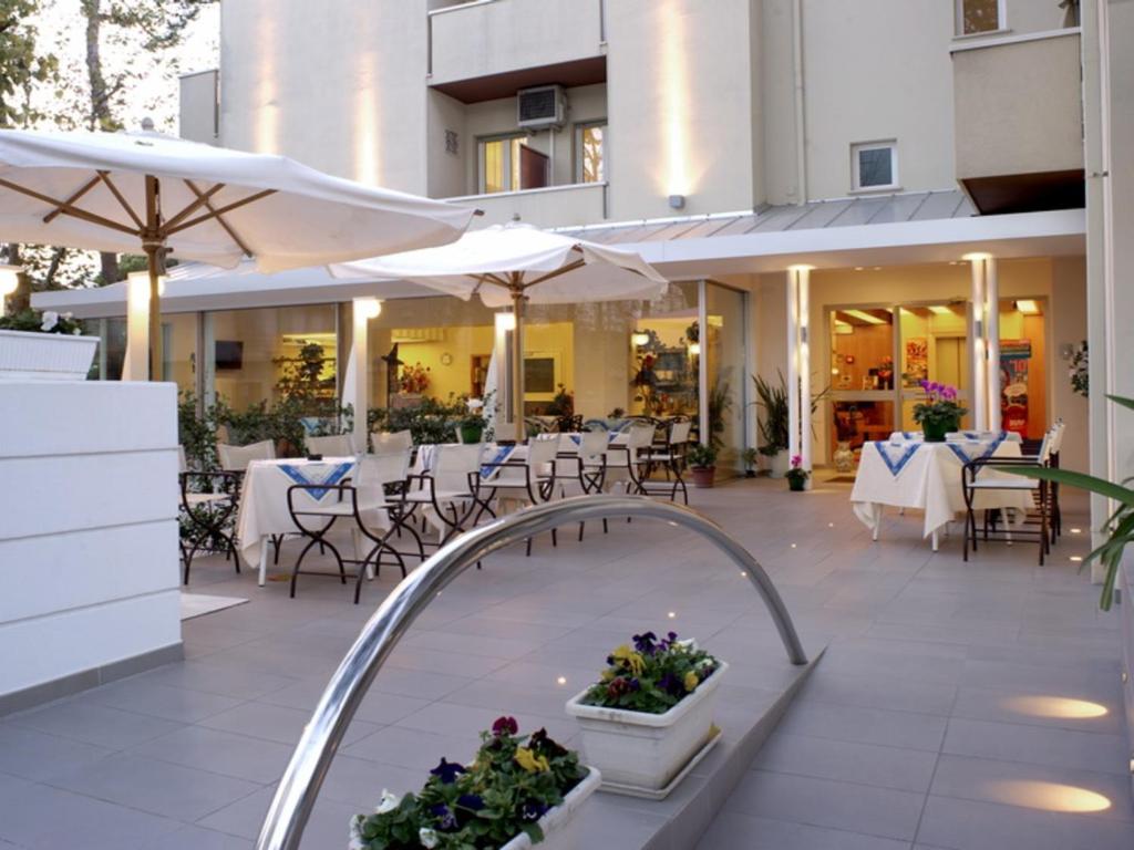 un patio al aire libre con mesas, sillas y sombrillas en Hotel Nives, en Riccione