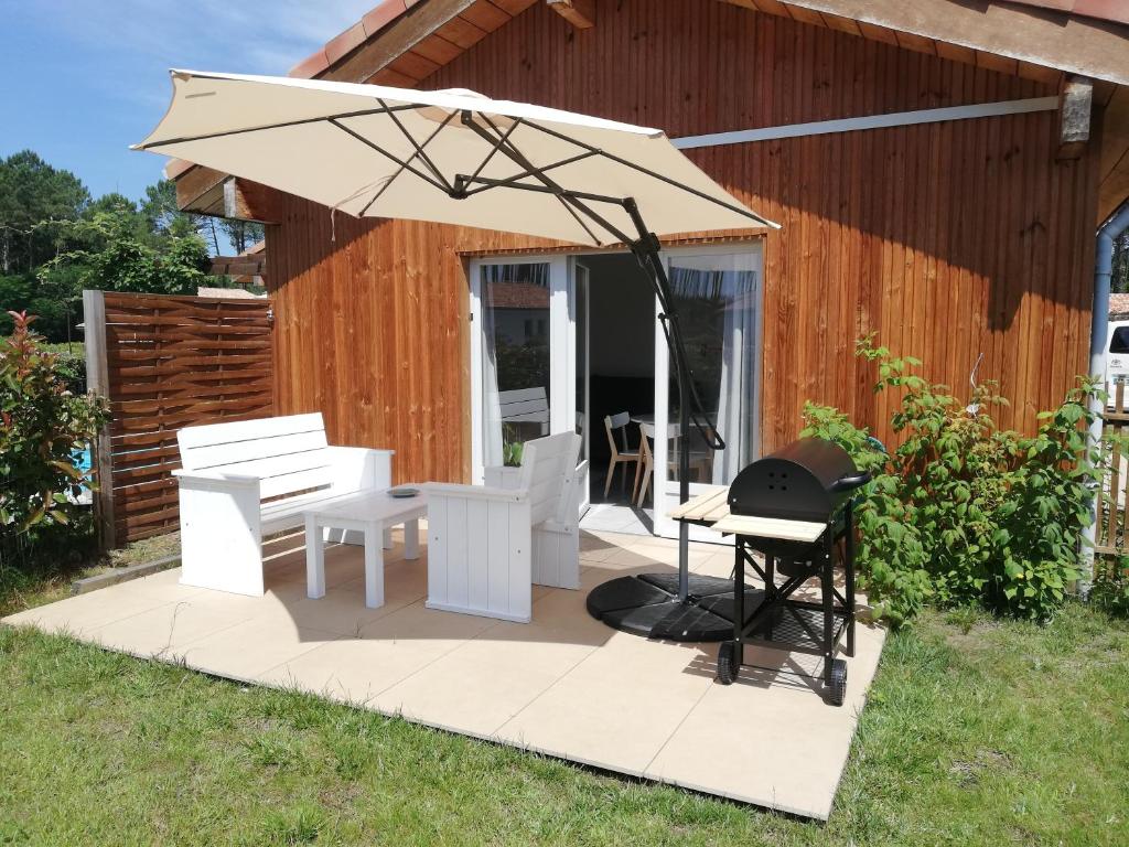 een patio met een parasol en een grill bij Appartement proche lac et plage in Léon