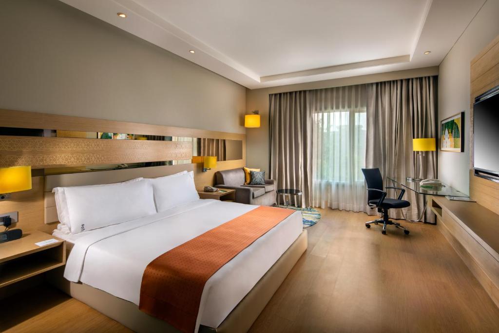 アグラにあるHoliday Inn Agra MG Road an IHG Hotelの大きなベッドとデスクが備わるホテルルームです。
