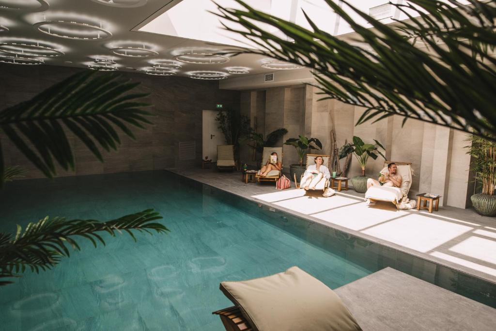 three people sitting in chairs next to a swimming pool at Hôtel 1770 & Spa in Le Pontet