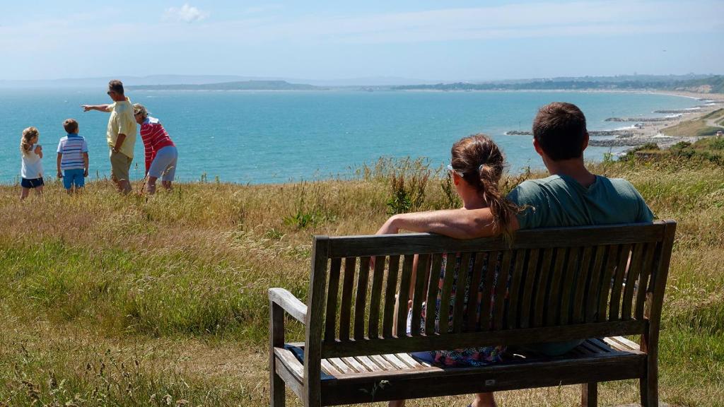 eine Gruppe von Menschen, die auf einer Bank sitzen und auf den Ozean blicken in der Unterkunft 17GD HOBURNE NAISH HOLIDAY PARK in Highcliffe