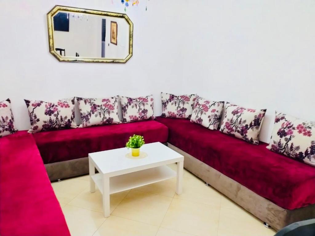 a red couch with a white table and a mirror at Appartement Charmant in Fnidek