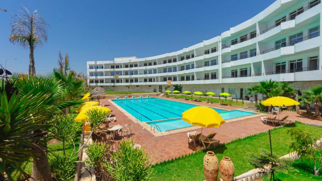 duży budynek z basenem i żółtymi parasolami w obiekcie Sables D'or Appart Hôtel w mieście Agadir