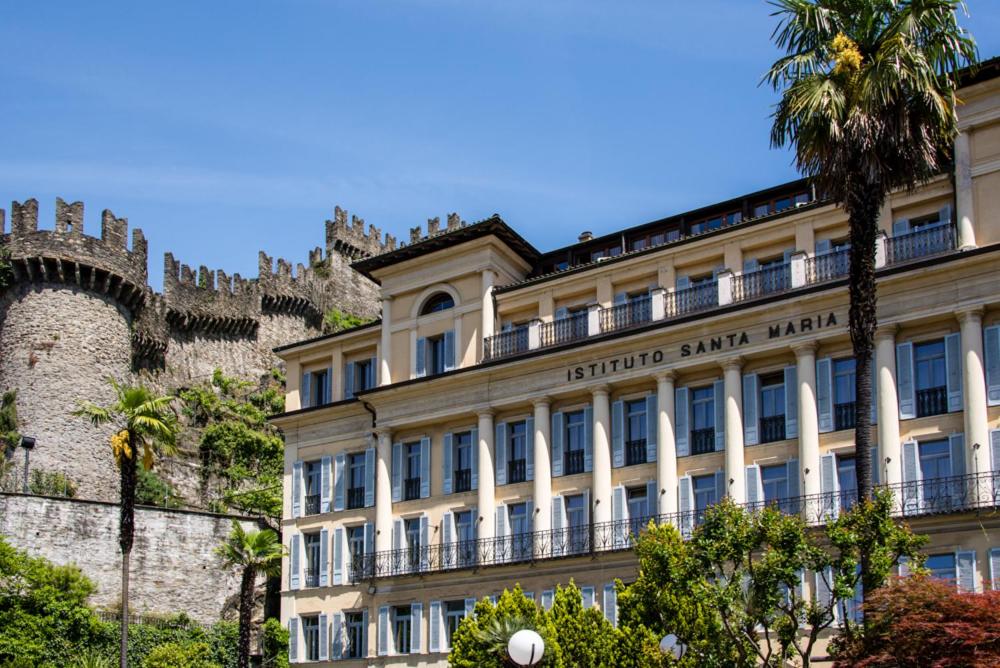 un edificio di fronte a un castello con una palma di Ostello Montebello - Bellinzona Youth Hostel a Bellinzona