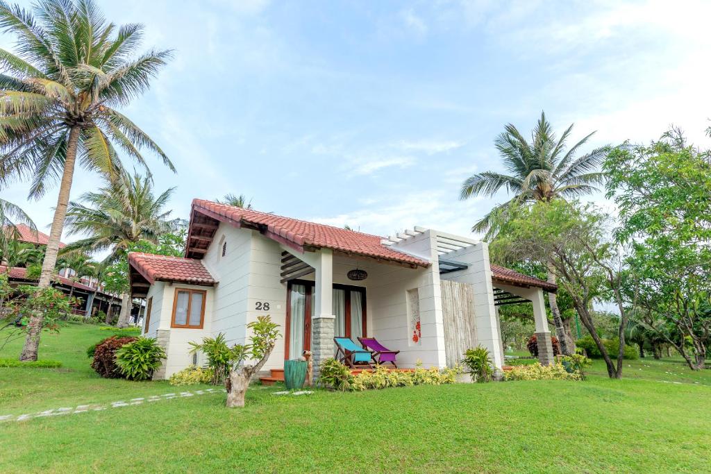 a white house with palm trees in a yard at Pax Ana Doc Let Resort & Spa in Ninh Hòa