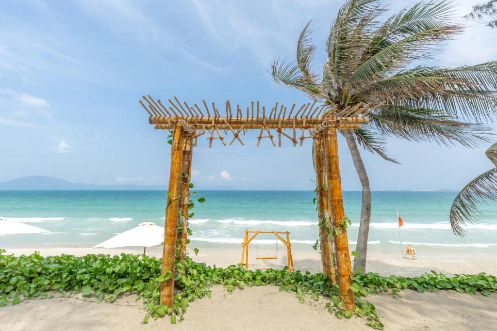 a wooden arch on the beach with a palm tree at Pax Ana Doc Let Resort & Spa in Ninh Hòa