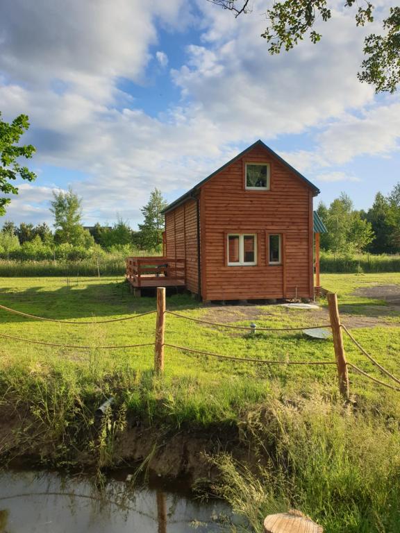 a small wooden house in a field with a fence at Uroczy domek (+ sauna) w Nowej Jedlance in Jedlanka Nowa