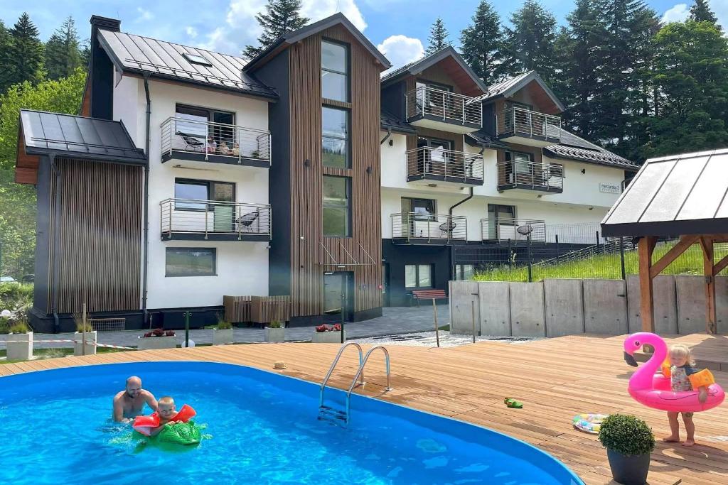 a man and two children in a swimming pool in front of a house at Aparthotel Narciarska 2 in Korbielów