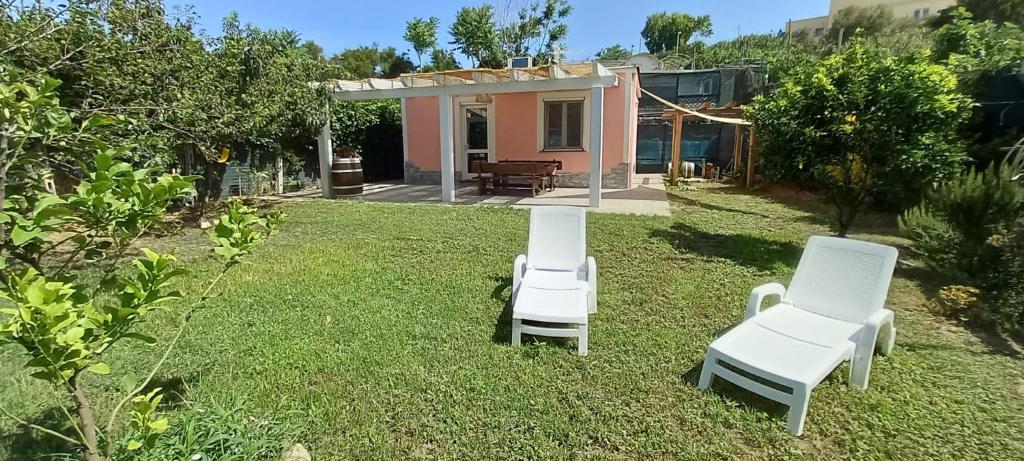 Deux chaises blanches assises sur l'herbe devant une maison dans l'établissement Casetta Furiana, à Procida