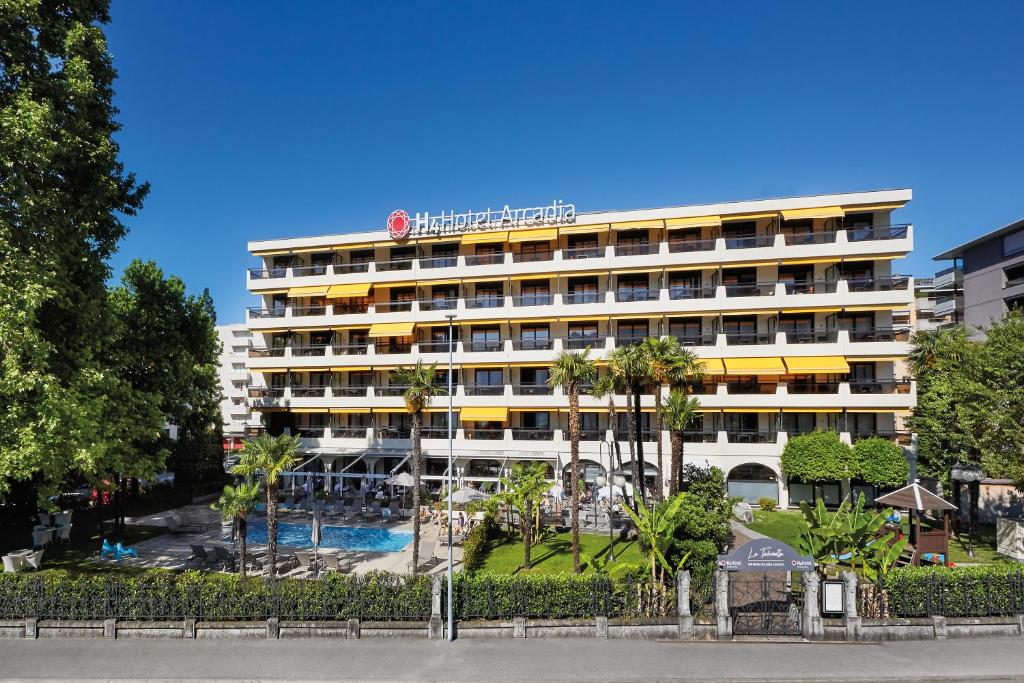 un edificio de hotel con piscina frente a él en H4 Hotel Arcadia Locarno en Locarno