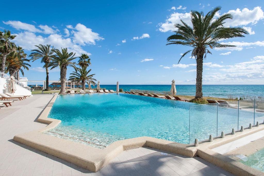 een zwembad met palmbomen en de oceaan bij Hotel Bel Azur Thalasso & Bungalows in Hammamet
