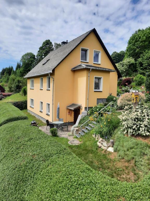 a yellow house on a hill with a garden at Ferienwohnung Tuchscherer in Cranzahl