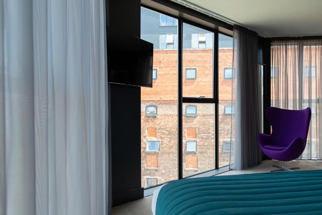 um quarto com uma cadeira roxa e uma grande janela em The Baltic Hotel em Liverpool