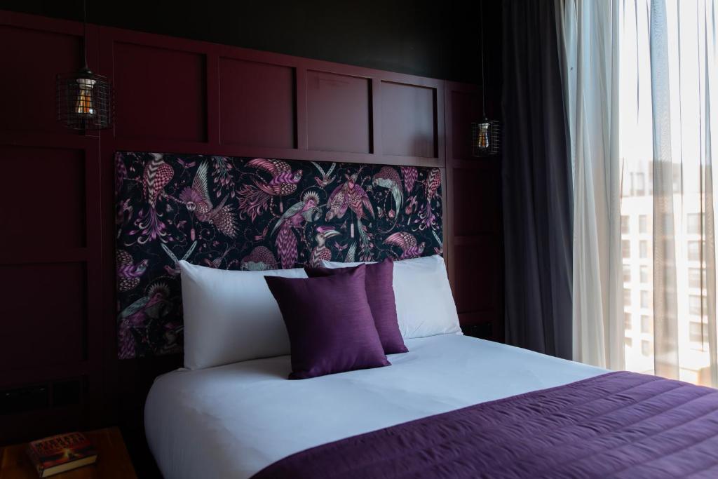 a bed with purple pillows in a room with a window at The Baltic Hotel in Liverpool