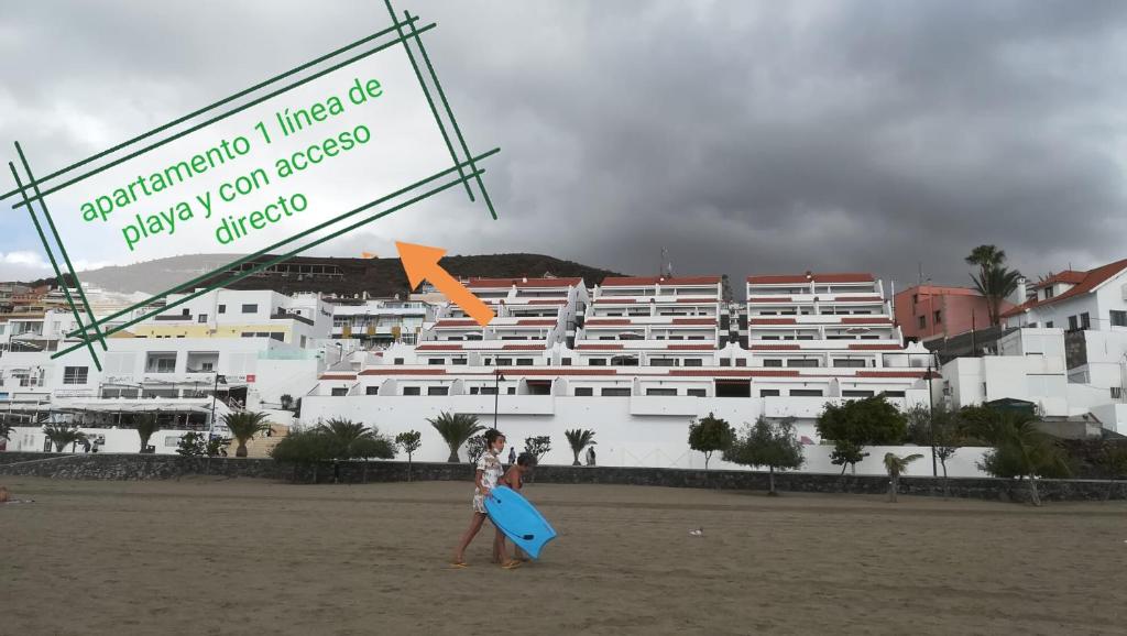 a woman walking on the beach with a blue surfboard at Apartamento en Los Cristianos in Los Cristianos