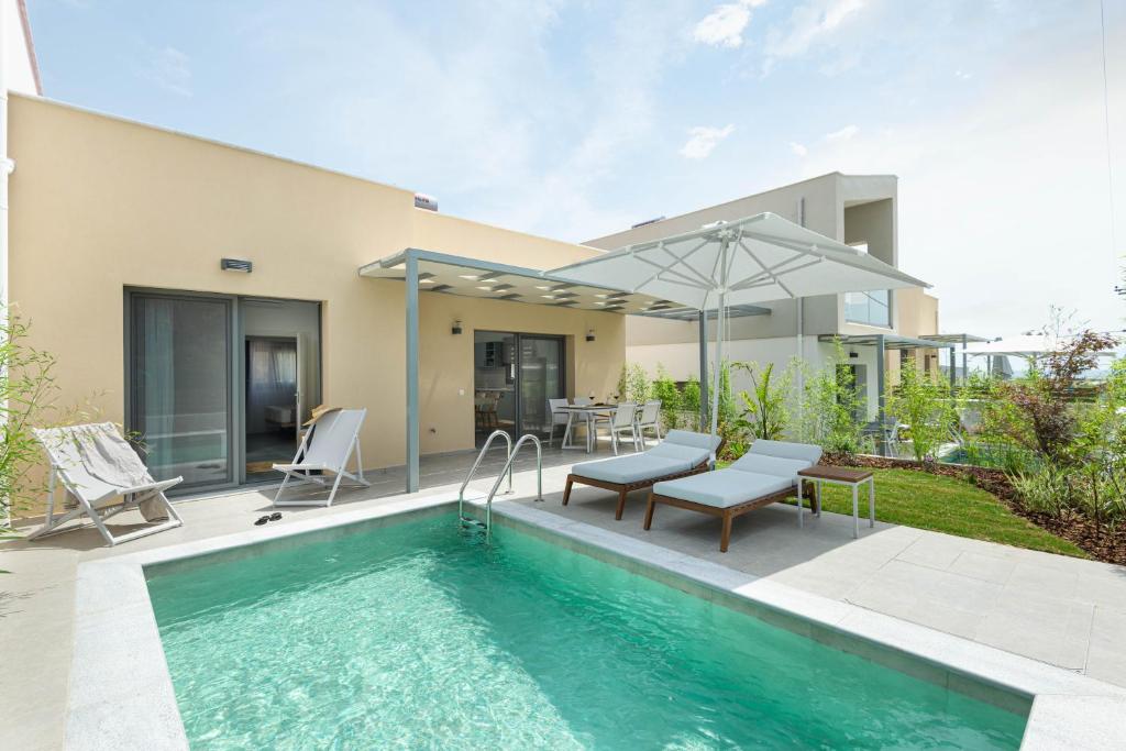 a swimming pool with chairs and an umbrella next to a house at Yuka Villas Collection in Iraklitsa