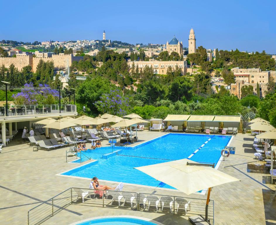 a swimming pool with umbrellas and a city in the background at The Inbal Jerusalem in Jerusalem