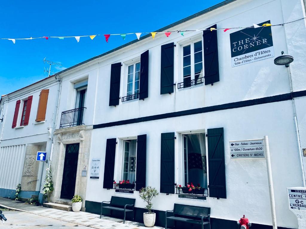een wit gebouw met zwarte luiken op een straat bij The Corner Properties in Noirmoutier-en-l'lle