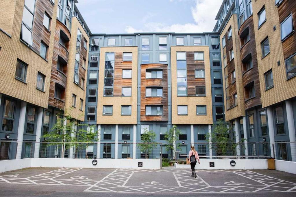 a woman walking in a courtyard in front of buildings at Modern Studios and Private Bedrooms with Shared Kitchen at Chapter Islington in London in London