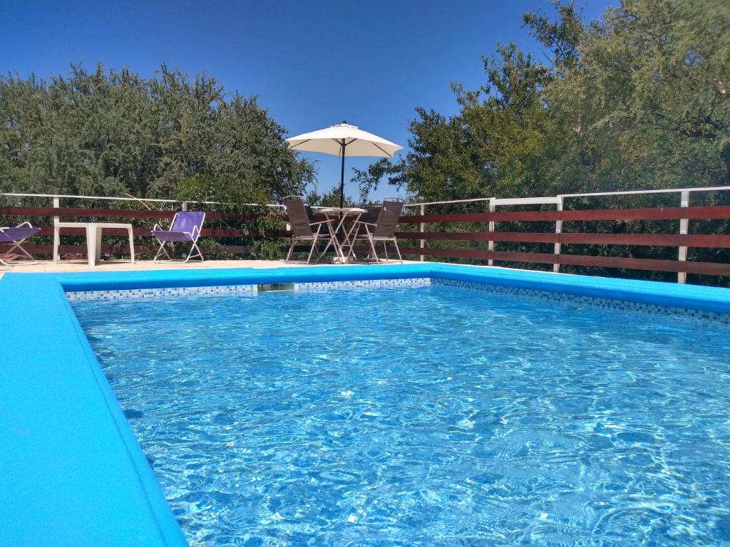 a blue swimming pool with chairs and an umbrella at Dorado del Sol in Merlo