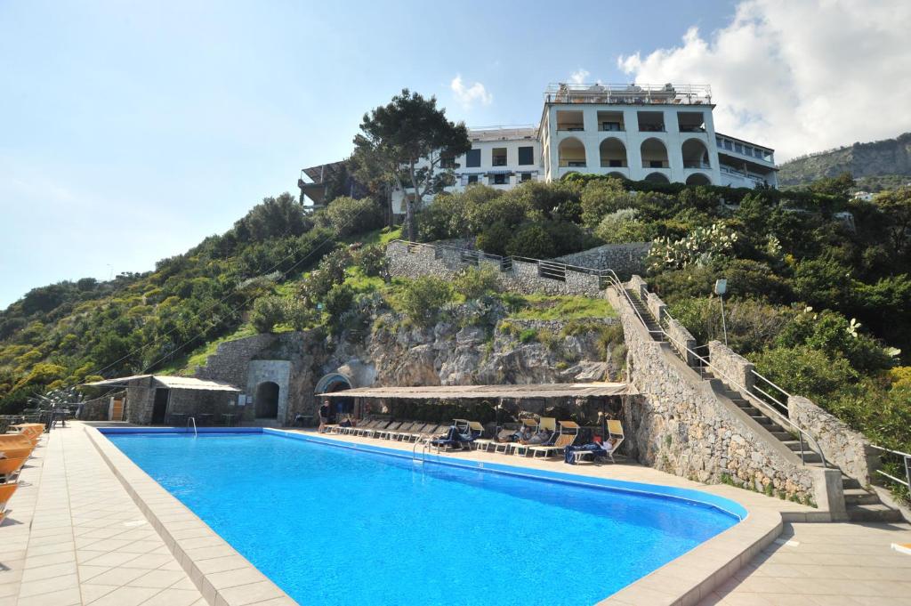 ein Schwimmbad mit einem Gebäude auf einem Hügel in der Unterkunft Hotel Belvedere in Conca dei Marini