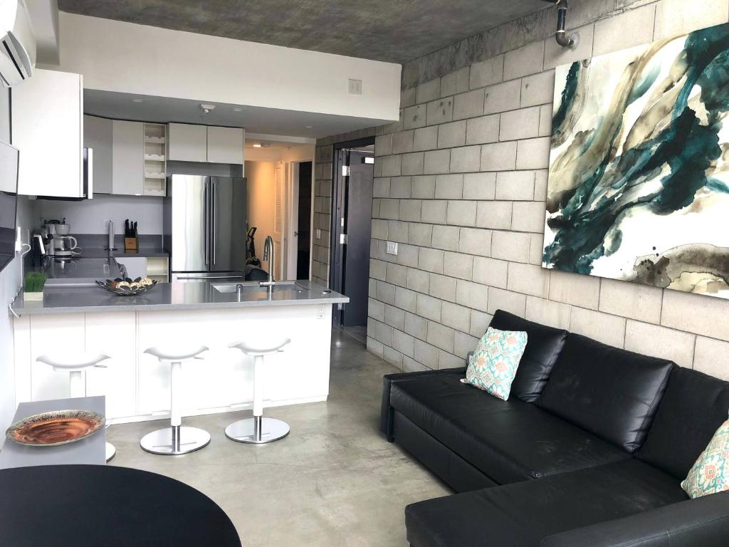 Una sala de estar con un sofá negro y una cocina. en Modern 2 Bdrm w/Parking in the Heart of Hillcrest, en San Diego