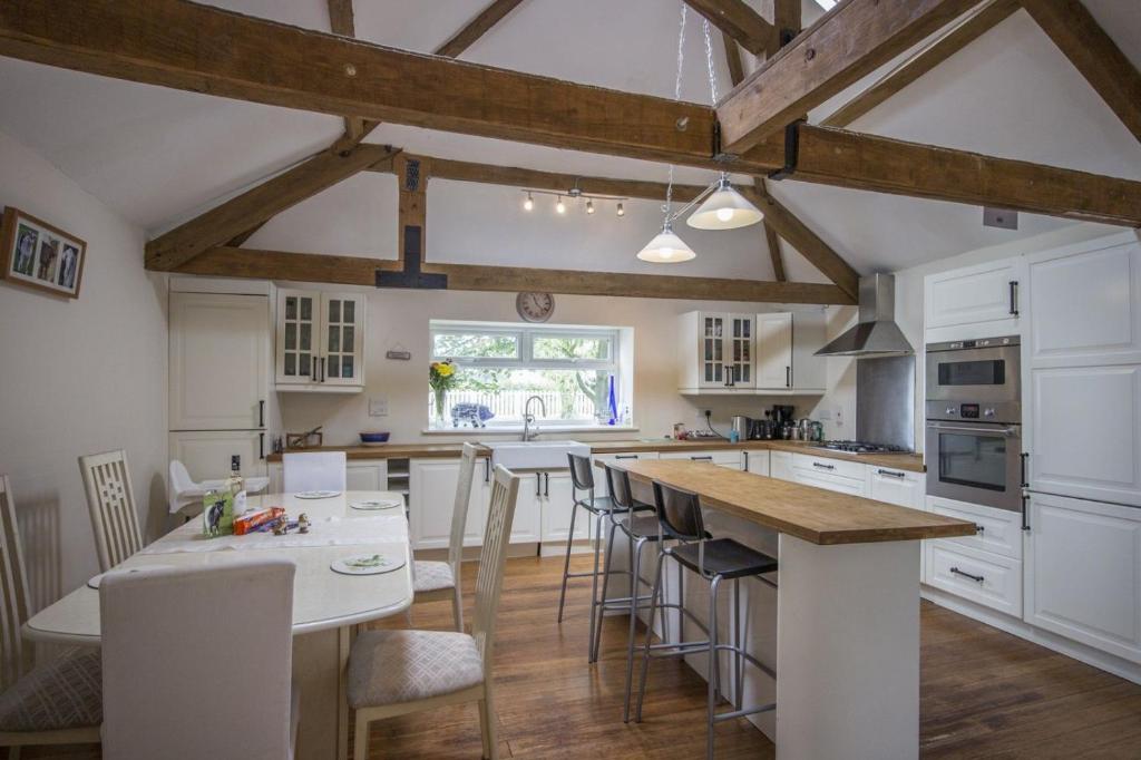 una cocina con armarios blancos y una gran isla con taburetes. en Stunning Barn Conversion next to Horse Field sleeps 10, en Morpeth