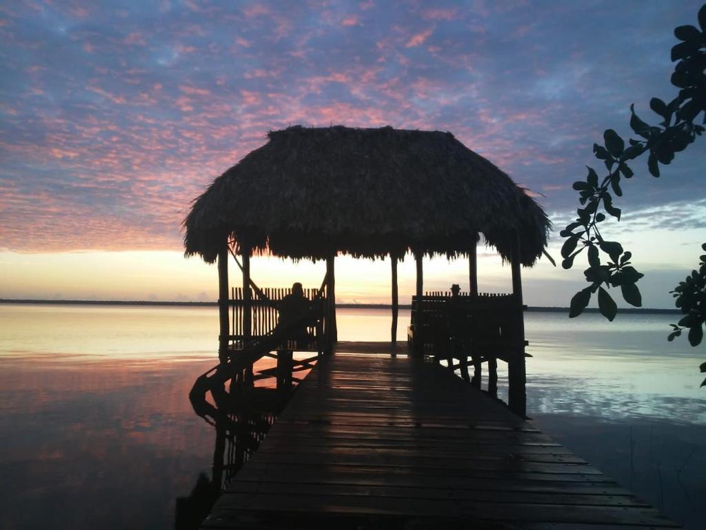 a pier with two chairs and a straw umbrella on the water at Villas Ecotucan in Bacalar
