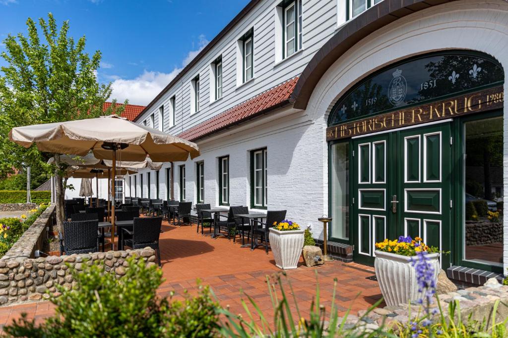 een patio met stoelen en een parasol naast een gebouw bij Hotel Historischer Krug in Oeversee