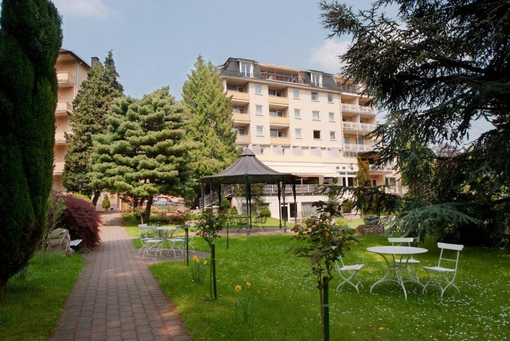 Parkhotel am Taunus في أوبروسل: حديقة بها شرفة وكراسي ومبنى