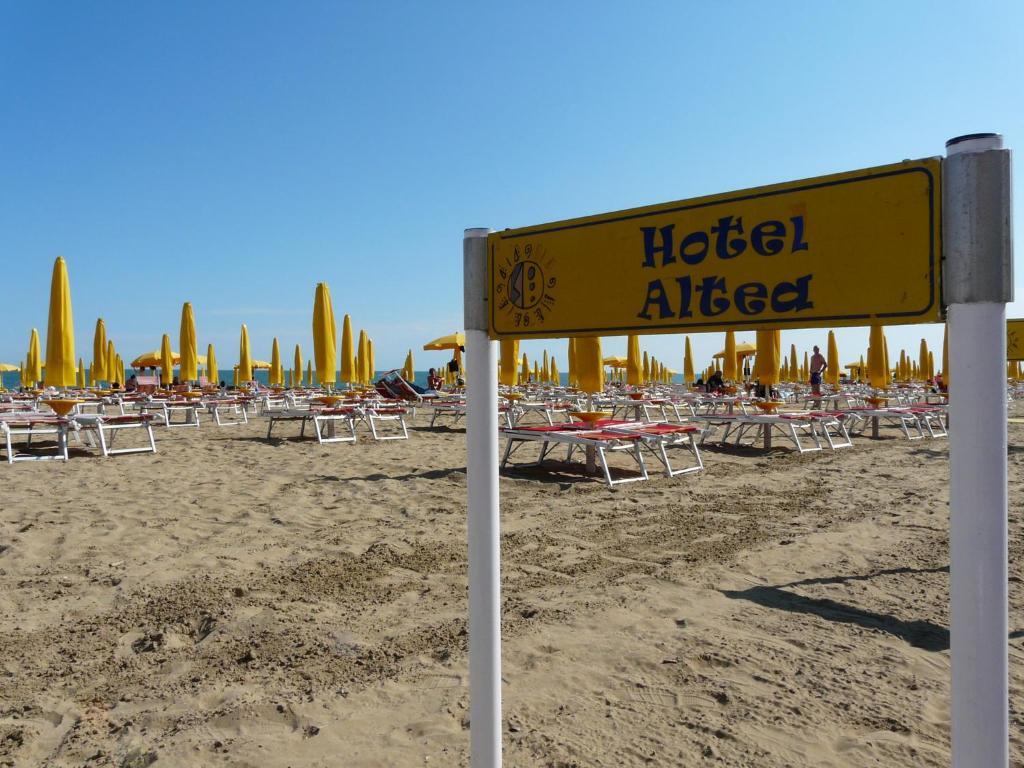 un cartello su una spiaggia con sedie e ombrelloni di Hotel Altea a Lido di Jesolo