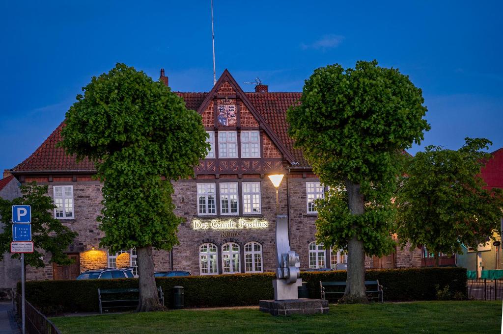 ein großes Backsteingebäude mit zwei Bäumen davor in der Unterkunft Det Gamle Posthus in Rønne