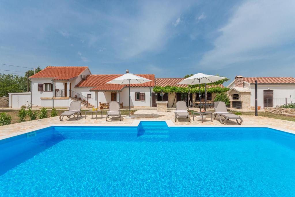 a pool in front of a house with chairs and umbrellas at Villa Vitis ZadarVillas in Oklaj