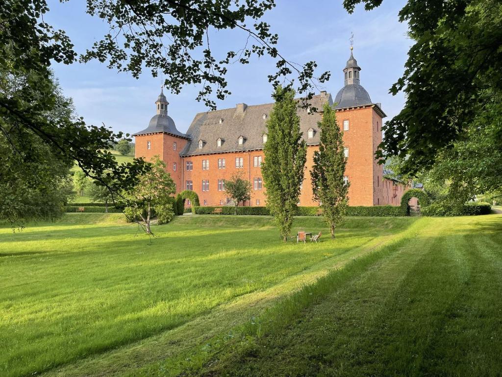 um grande edifício de tijolos vermelhos com árvores num campo em Ferienwohnungen Jagdschloss Adolphsburg em Kirchhundem