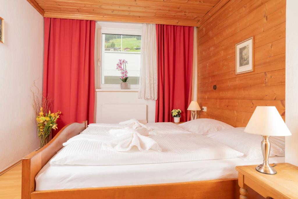 um quarto com uma cama branca com cortinas vermelhas e uma janela em Appartements Bernhofer em Saalbach-Hinterglemm